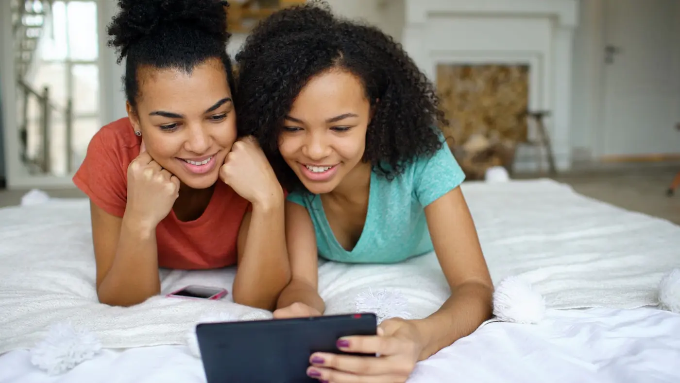 Two teenage girls smiling at a tablet together