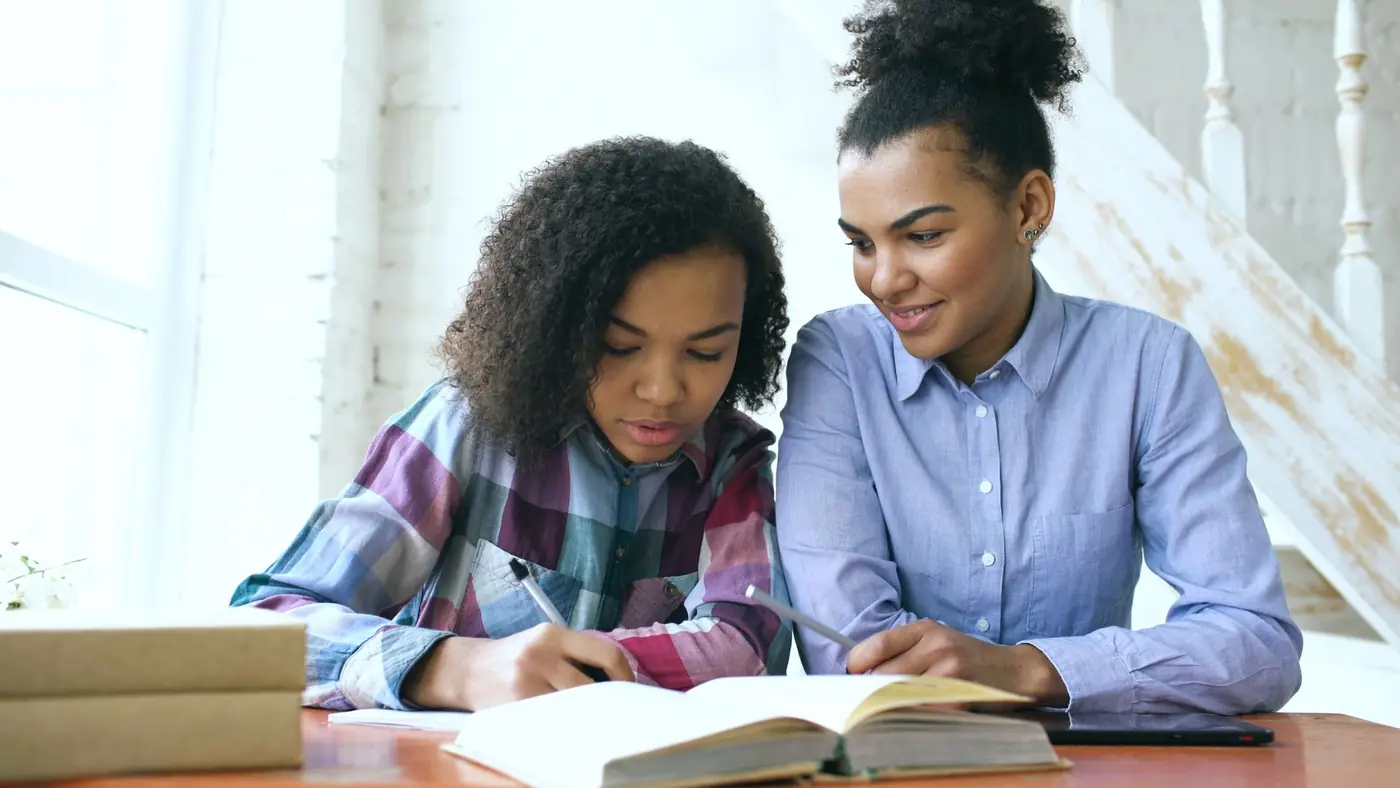 An adult helping a teenage girl with her studies at the table